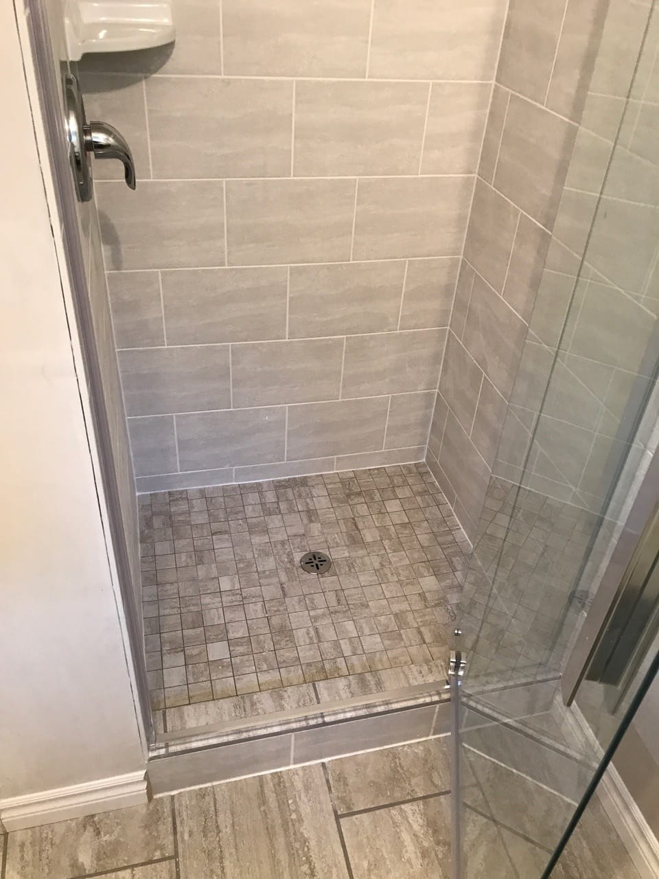 Narrow tiled shower with mosaic floor and glass door