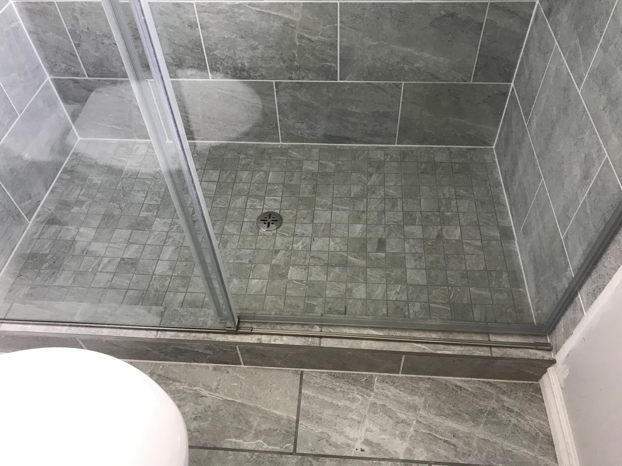 Grey mosaic shower floor with centre drain and sliding glass door